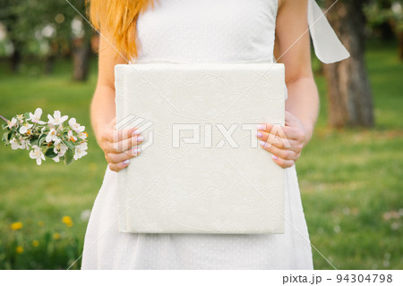 A white-covered wedding photo album is held by a woman in a white dress 94304798
