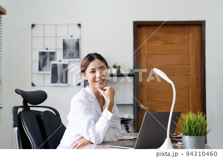 Smiling asian female doctor with laptop computer in her office. Friendly medical professional with tablet computer in clinic. Smiling asian female doctor with laptop computer in her office. Friendly medical professional with tablet computer in clinic. 94310460
