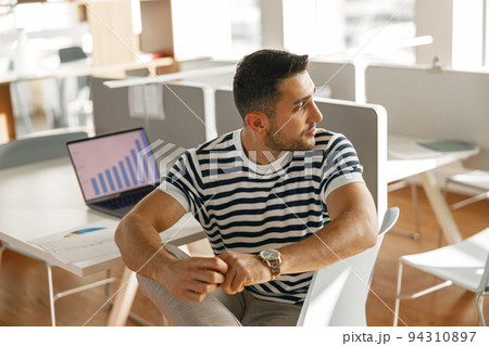 Businessman in casual clothes working laptop while sitting in modern office on colleagues background Businessman in casual clothes working laptop while sitting in modern office on colleagues background 94310897