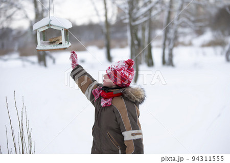 Boy in winter puts bread in the bird feeder. Feed the birds in winter. 94311555