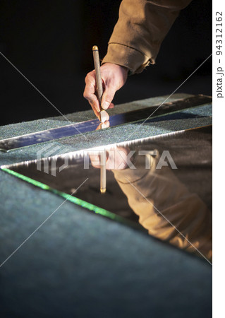 The hand of a working man cuts a mirror with a glass cutter. 94312162