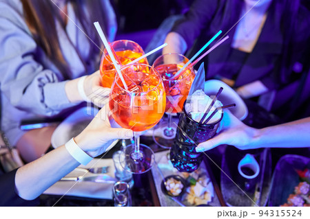 Girls in a nightclub clink glasses with alcoholic drinks 94315524