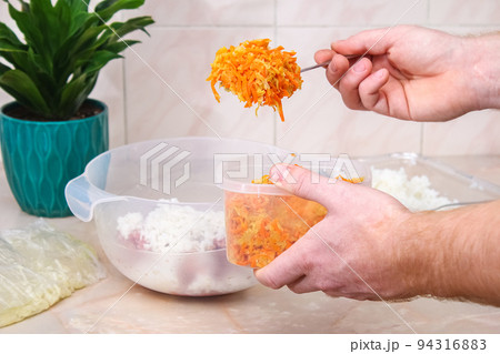A man adds fried onions and carrots to minced meat 94316883