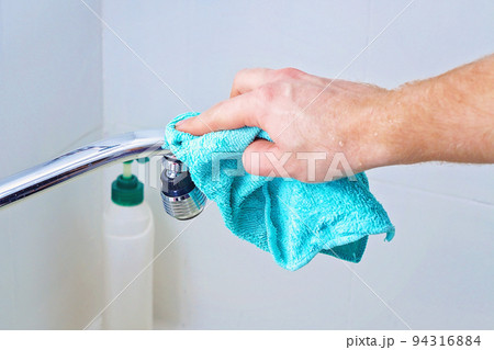 A man wipes a mixer tap, faucet with a rag 94316884