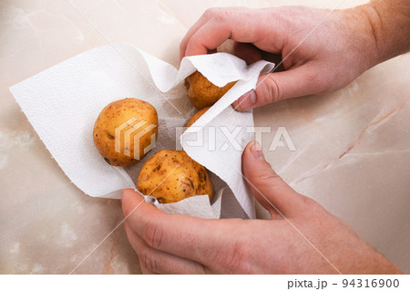 A man dries raw, washed potatoes with paper towels 94316900