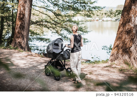 Rear view of casualy dressed mother walking with baby stroller in city park. Family, child and parenthood concept. 94320516