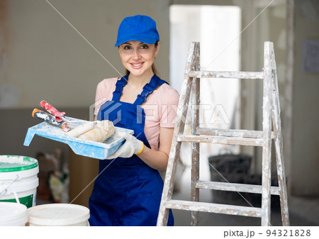 Portrait of woman painter in blue overall with paint roller 94321828