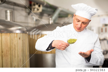 Experienced male brewer holding glass and looking at hops pellets Experienced male brewer holding glass and looking at hops pellets 94322363