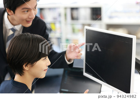 先輩からプログラミングのレクチャーを受ける笑顔の女性エンジニア_1 94324982