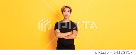 Portrait of serious-looking confident asian guy in black t-shirt, cross arms chest, standing yellow background 94325717
