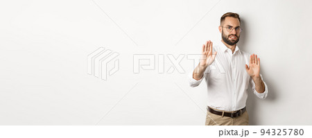 Displeased man rejecting something disturbing, showing stop sign and declining, cringe from aversion, standing over white background Displeased man rejecting something disturbing, showing stop sign and declining, cringe from aversion, standing over white background 94325780