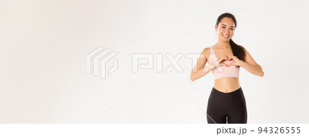 Sport, wellbeing and active lifestyle concept. Smiling asian woman in activewear, sportswoman showing heart gesture, enjoy workout in her favorite gym, using product she loves, white background Sport, wellbeing and active lifestyle concept. Smiling asian woman in activewear, sportswoman showing heart gesture, enjoy workout in her favorite gym, using product she loves, white background 94326555