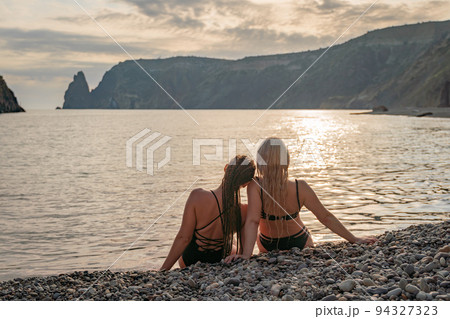 Two beautiful lgbt lesbian female friends relax and happy at the beach sitting on the sand wearing swimsuit. Travel and sea on holiday vacation. 94327323
