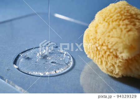 A natural sponge and a drop of gel or shampoo on a blue background. A natural sponge and a drop of gel or shampoo on a blue background. 94329329