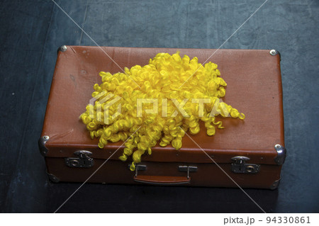 Retro suitcase with a clown wig on a dark floor. 94330861