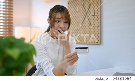 Shocked young woman holding and looking at credit card with excited and surprised. Online shopping, internet banking concept Shocked young woman holding and looking at credit card with excited and surprised. Online shopping, internet banking concept 94331064