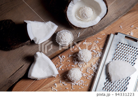 Close up of coconut with white pulp, grater with coconut chip and white candies on wooden background.. Close up of coconut with white pulp, grater with coconut chip and white candies on wooden background.. 94331223