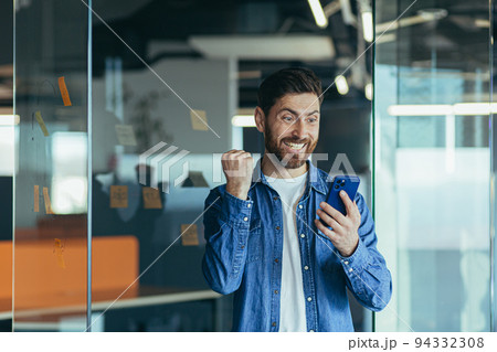 Excited happy business man with a beard, a professional winner, celebrating success by reading good news on a smartphone, feeling excited about mobile messaging 94332308