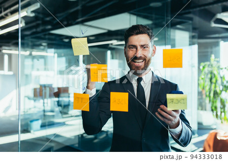 Portrait of a successful businessman near a glass board with tasks, the man fulfilled his plan on time, rejoices and celebrates victory 94333018
