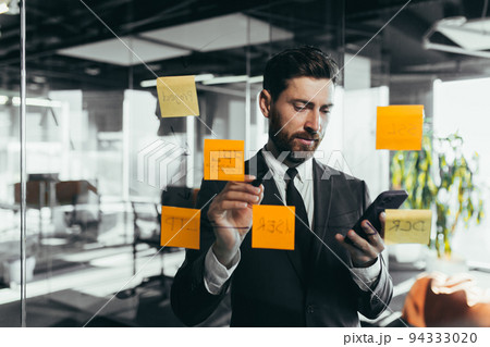 Successful businessman rewrites a task on a glass board with colored stickers, from phone and tablet Successful businessman rewrites a task on a glass board with colored stickers, from phone and tablet 94333020