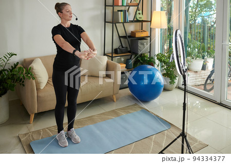 Mature fitness instructor running online class for clients and explaining how to stretch hands to warm up Mature fitness instructor running online class for clients and explaining how to stretch hands to warm up 94334377