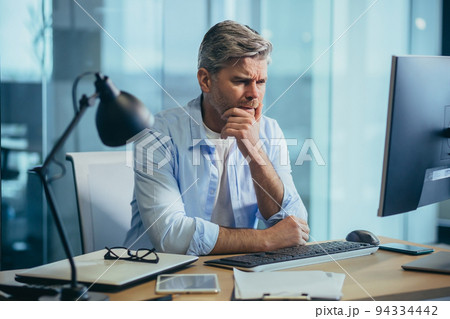 Business man in thought, solves important issues, and makes choices, gray-haired businessman works at computer in modern office Business man in thought, solves important issues, and makes choices, gray-haired businessman works at computer in modern office 94334442