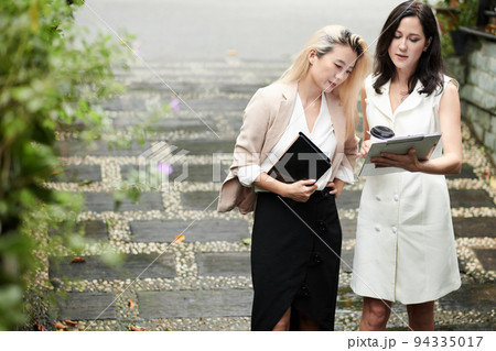 Serious female entrepreneurs standing outdoors and discussing contract details before meeting Serious female entrepreneurs standing outdoors and discussing contract details before meeting 94335017