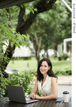 Portrait of smiling young female entrepreneur working on laptop at table in city park Portrait of smiling young female entrepreneur working on laptop at table in city park 94335078