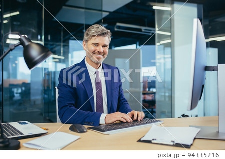 Portrait of a successful experienced gray-haired broker man, business man working in a modern office, looking at the camera rejoices and smiles 94335216