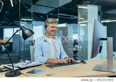 Portrait of a successful businessman, gray-haired man talking to colleagues on a video call, using a headset, smiling and rejoicing 94335469