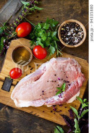 Fresh raw meat. Raw pork meat fillet with tomatoes, olive oil, spices and fresh basil on rustic wooden table. Top view flat lay background. Copy space. Fresh raw meat. Raw pork meat fillet with tomatoes, olive oil, spices and fresh basil on rustic wooden table. Top view flat lay background. Copy space. 94335880