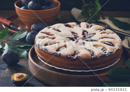 Delicious dessert plum pie, sweet delicious holiday cake with plums on wooden table. Toned image. Delicious dessert plum pie, sweet delicious holiday cake with plums on wooden table. Toned image. 94335932