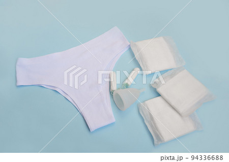 White pants with sanitary napkins, tampons, menstrual cup on blue background. Concept of critical days, menstruation. White pants with sanitary napkins, tampons, menstrual cup on blue background. Concept of critical days, menstruation. 94336688