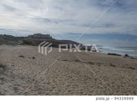 View of empty Praia da Ilha do Pessegueiro sand beach with ocean waves and small fortress and restaurant at Rota Vicentina coast near Porto Covo, Portugal. 94339999