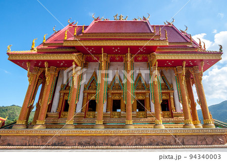 A beautiful Buddhist temple with gilded columns and an ornament and a red roof. Sacred plots are molded from clay below. 94340003