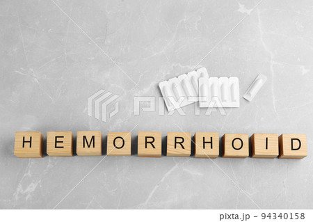 Wooden cubes with word HEMORRHOID and suppositories on grey marble table, flat lay 94340158