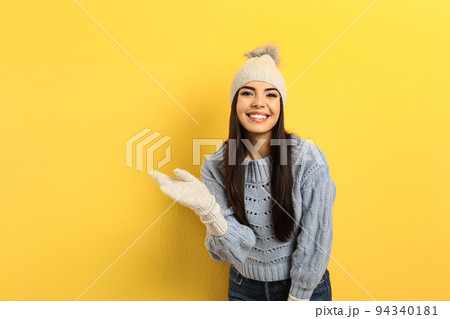 Happy young woman in warm clothes on yellow background. Winter vacation 94340181