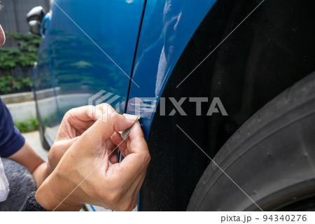 青い車のボディについた擦り傷を修理しようとしているシニア男性の手元 94340276