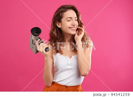 Beautiful young woman with vintage video camera on crimson background 94341259