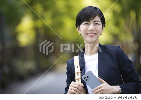 スマートフォンを片手にオフィス街を歩くビジネスウーマン スマートフォンを片手にオフィス街を歩くビジネスウーマン 94342436