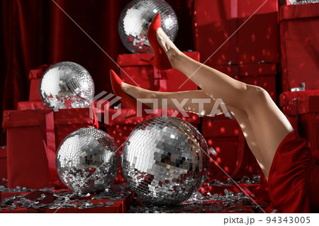 Woman sitting near disco balls on red Christmas gifts indoors, closeup 94343005