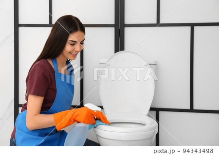 Young woman cleaning toilet bowl in bathroom Young woman cleaning toilet bowl in bathroom 94343498