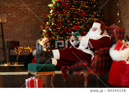 Santa Claus reading book near decorated Christmas tree indoors Santa Claus reading book near decorated Christmas tree indoors 94344158