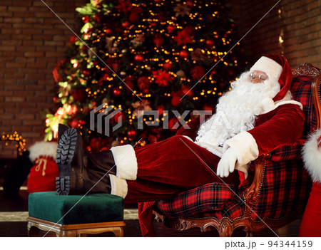 Santa Claus resting in armchair near decorated Christmas tree indoors 94344159
