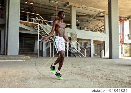 Black young sportsman working out with jumping rope outdoors 94345322