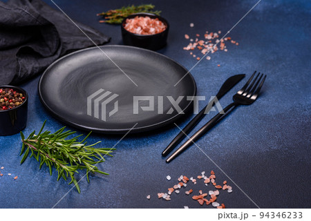 An empty black plate on a dark concrete background with spices and herbs An empty black plate on a dark concrete background with spices and herbs 94346233