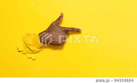 African american male hand pointing aside on virtual object or text, gesturing through the torn yellow paper background 94350604