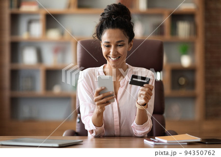 Positive businesswoman shopping online from office, using smartphone 94350762