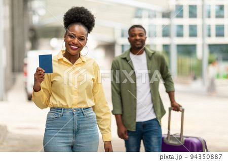 Joyful African Travelers Couple Showing Passport Standing At Airport Outdoors 94350887