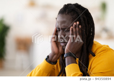 Closeup Shot Of Stressed Black Young Man Suffering From Headache At Home Closeup Shot Of Stressed Black Young Man Suffering From Headache At Home 94350894